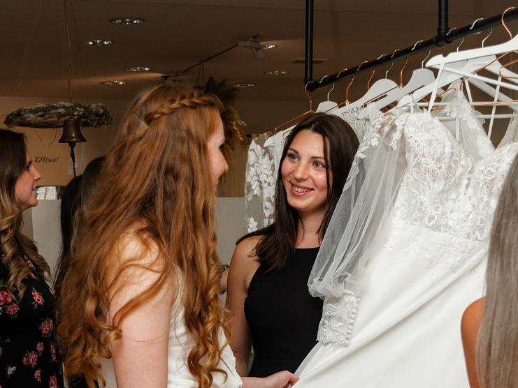 Brautberatung bei Clebeo Love Frau, die Brautkleid von Mitarbeiterin gezeigt bekommt im Brautladen